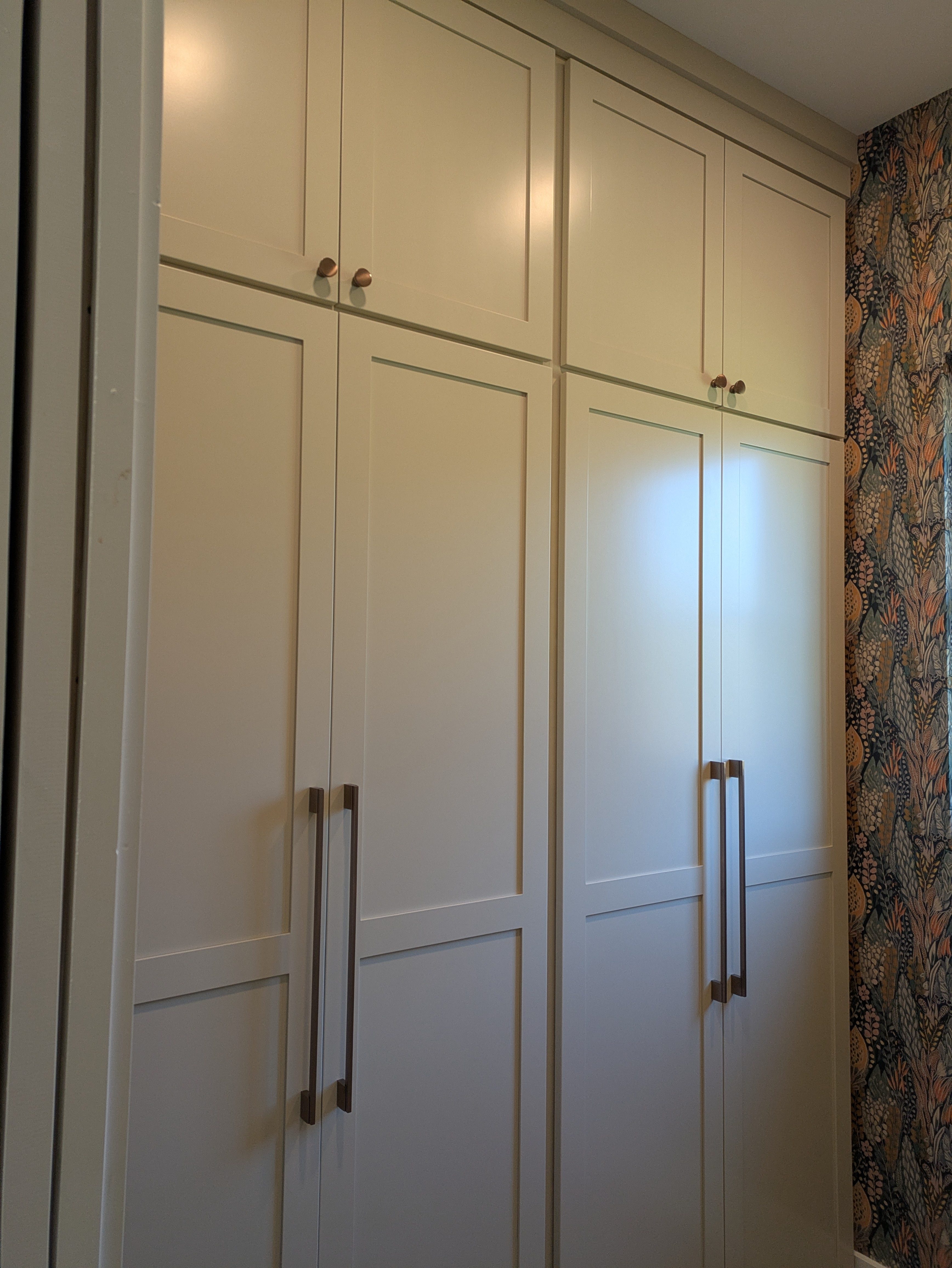 Tall white shaker cabinets with floral wallpaper accent wall